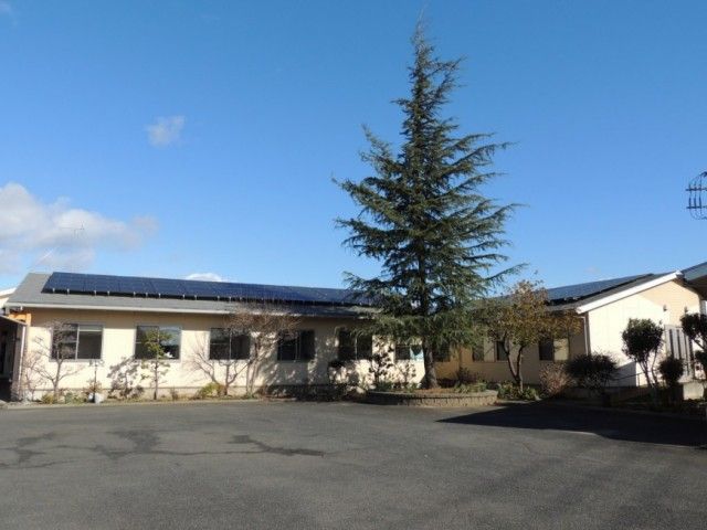 緑豊かな環境にある、平屋建ての建築物。白い外壁三角屋根。