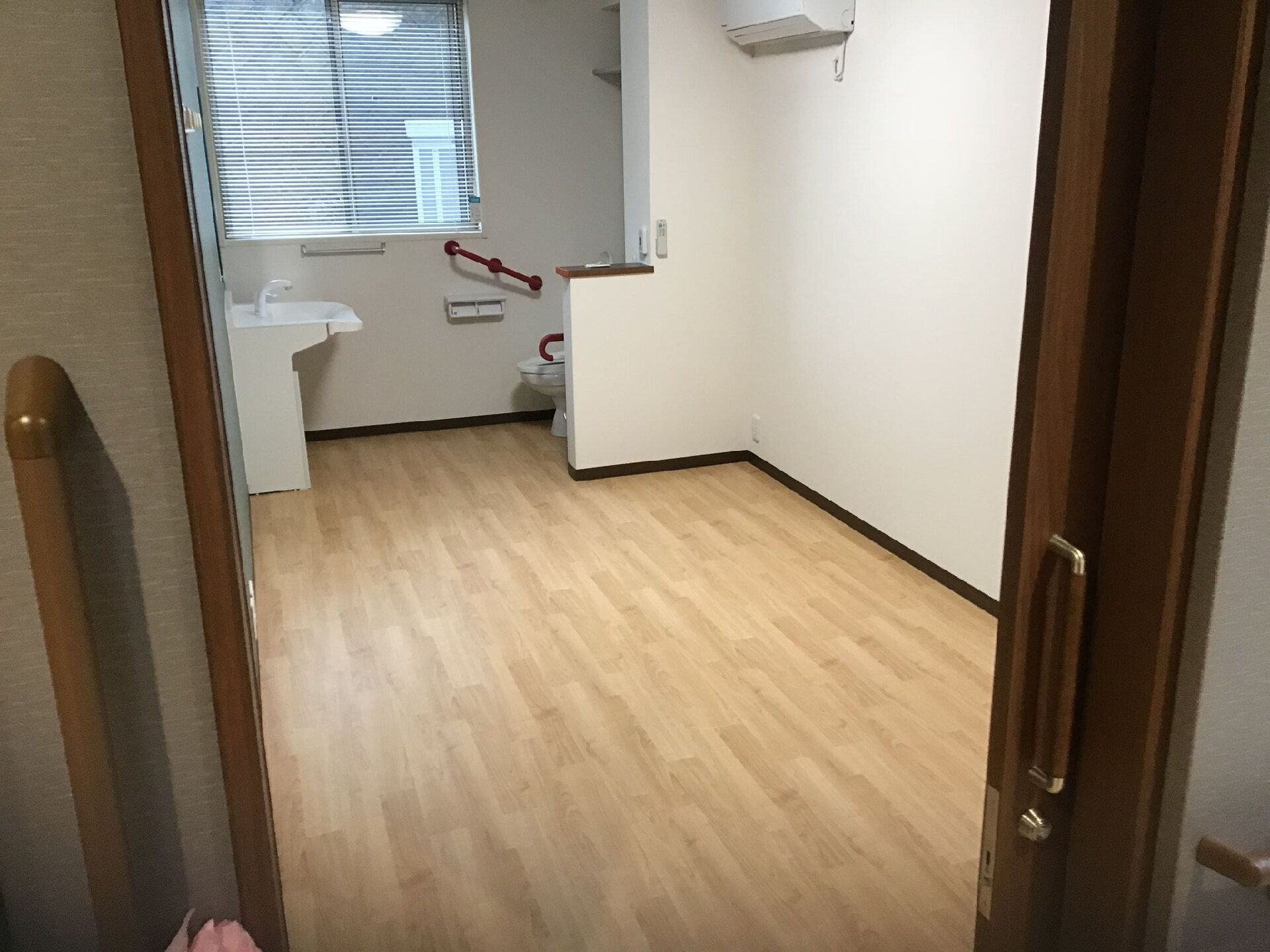 トイレや洗面所が奥の窓のそばに設置されている。フローリングの部屋には家具や家電は置かれていない。