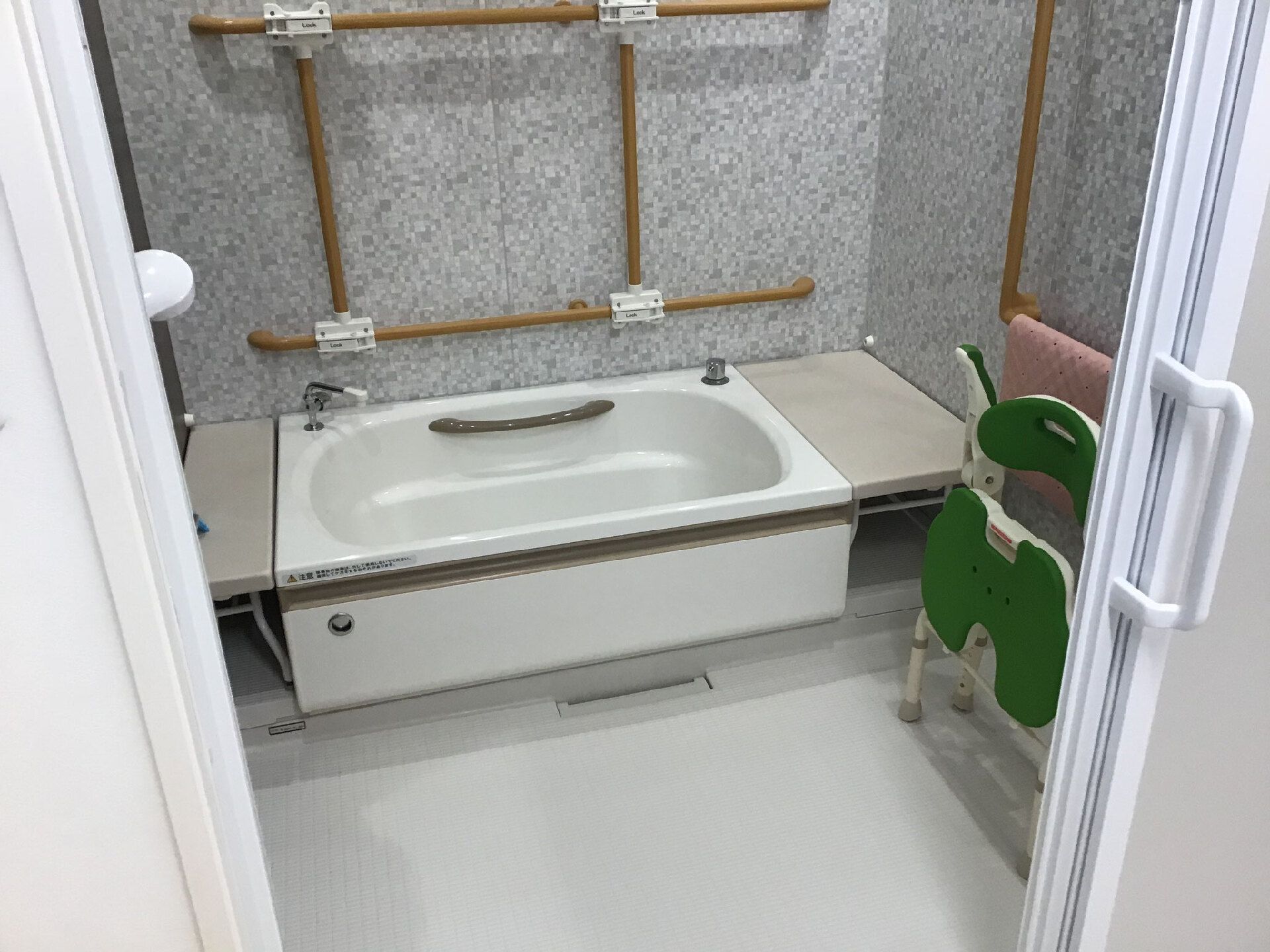 ブラウンの手すりがたくさん付いた一人用の浴槽が設置された浴室にはシャワーやシャワーチェアもある。