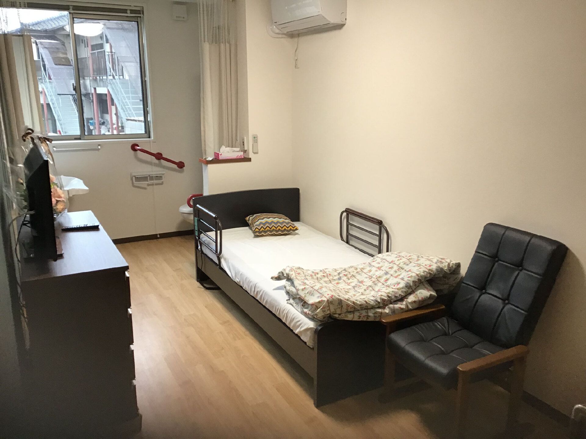 寝具付きのベッドや一人用のいすが置かれたフローリングの部屋の一番奥にトイレや洗面所もある。