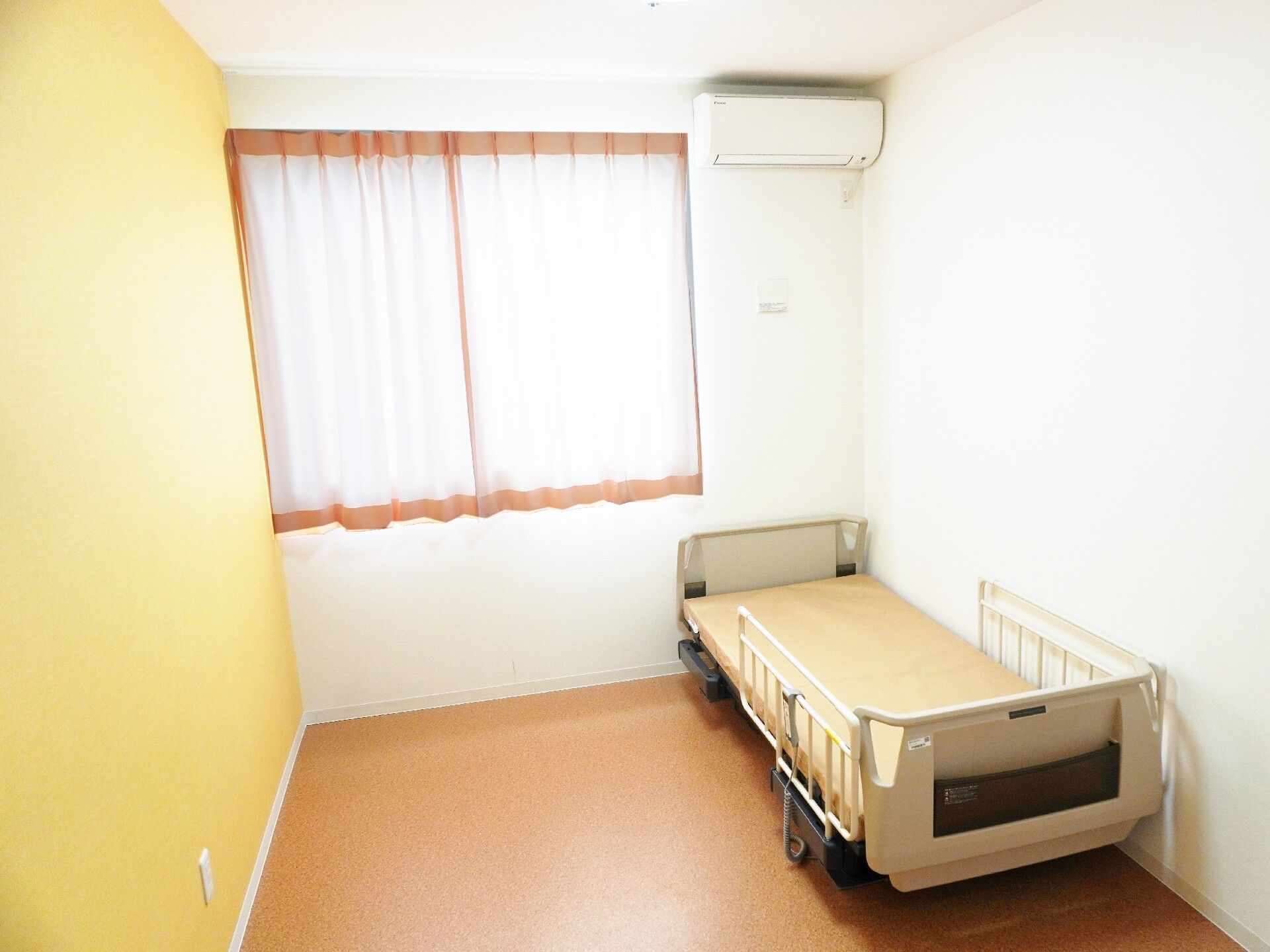 エアコンがあり、柵付きのベッドが置いてある黄色い壁紙のお部屋