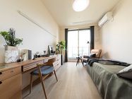 寝具付きのベッドが壁際に置かれたフローリングの居室には、エアコンやカーテン付きの窓もあり、テレビや家具、観葉植物などもある。