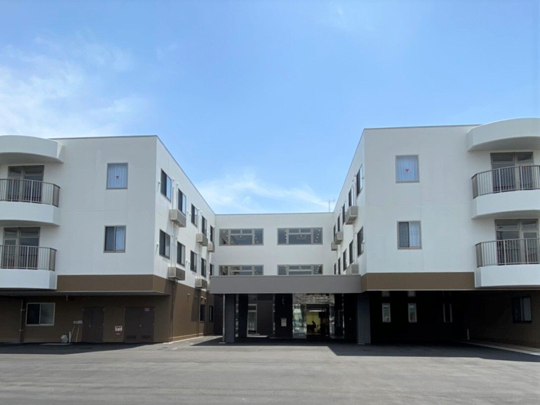 白とブラウンの3階建ての建物が2棟あり、敷地内には駐車場も完備。人の行き来も多い。
