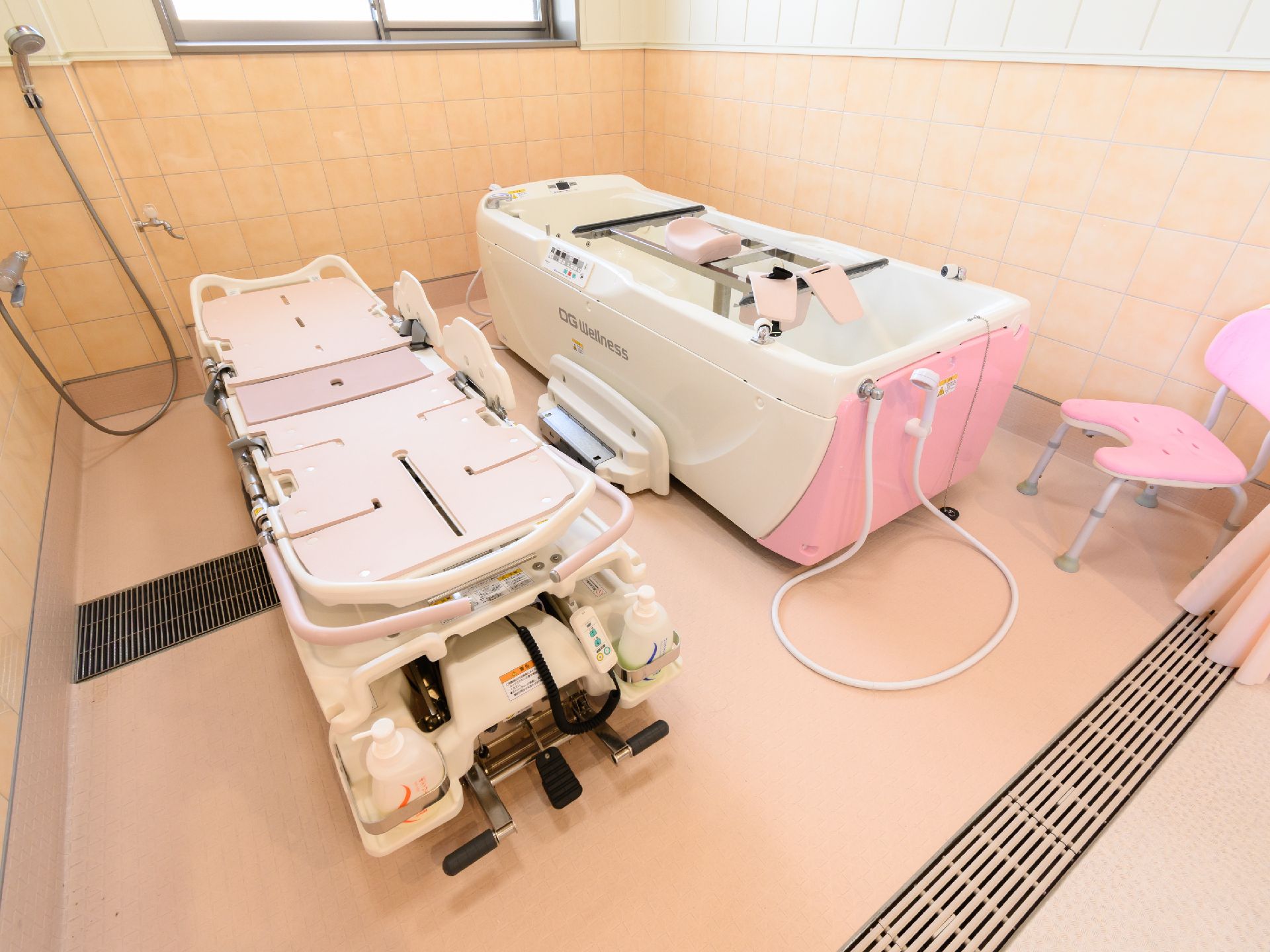 ピンクのタイル調の部屋に置かれたストレッチャーと機械浴用の浴槽
