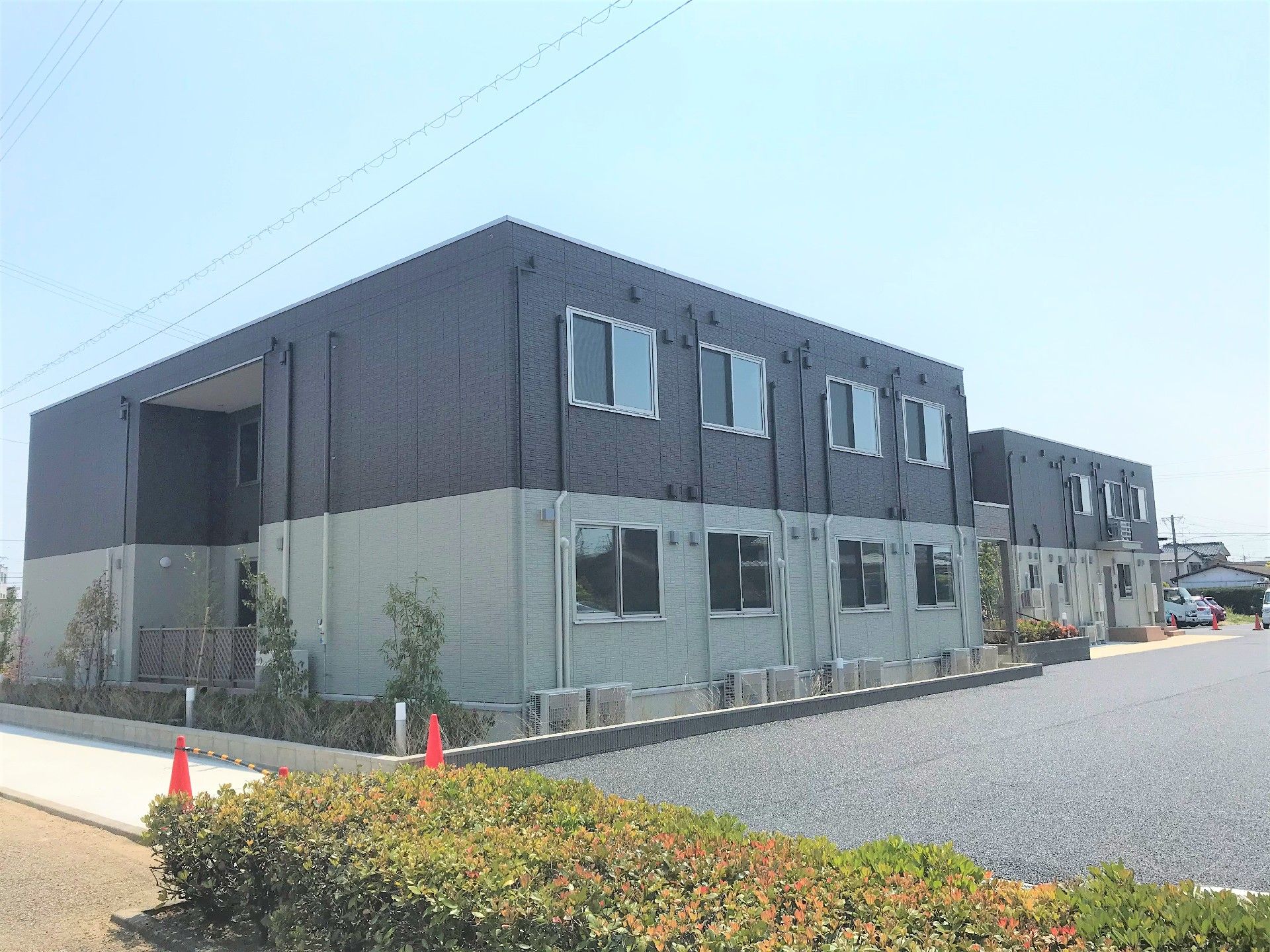2階建てのグレー系の建物は横に長く窓がたくさんあり、建物周辺にはたくさんの木もある。