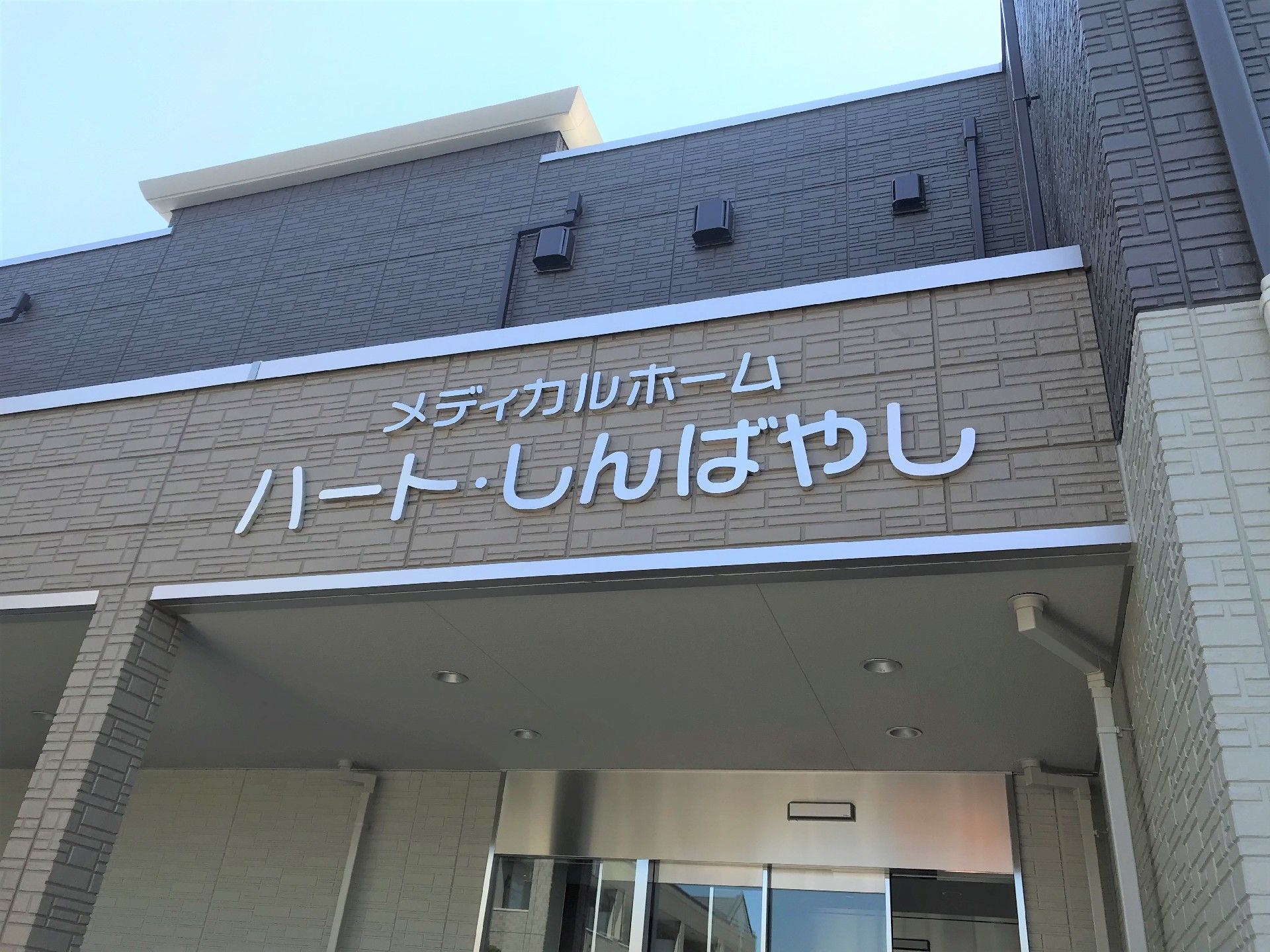 2階建てで駐車スペースが付き、フロアごとに外壁の色が異なる。周囲には木も植えられている。