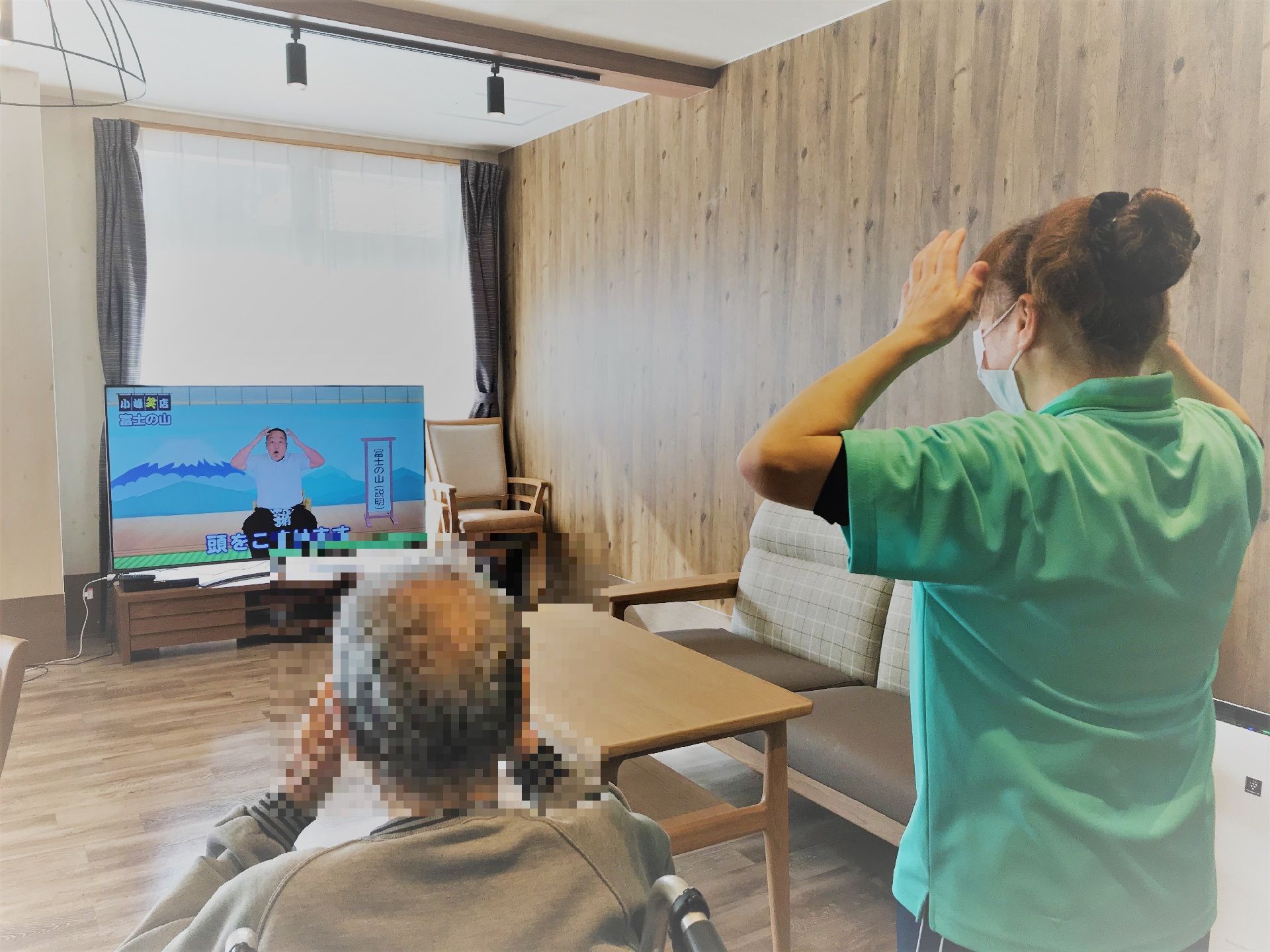 テレビを観ながら座って体操をする高齢者と指導をするスタッフ