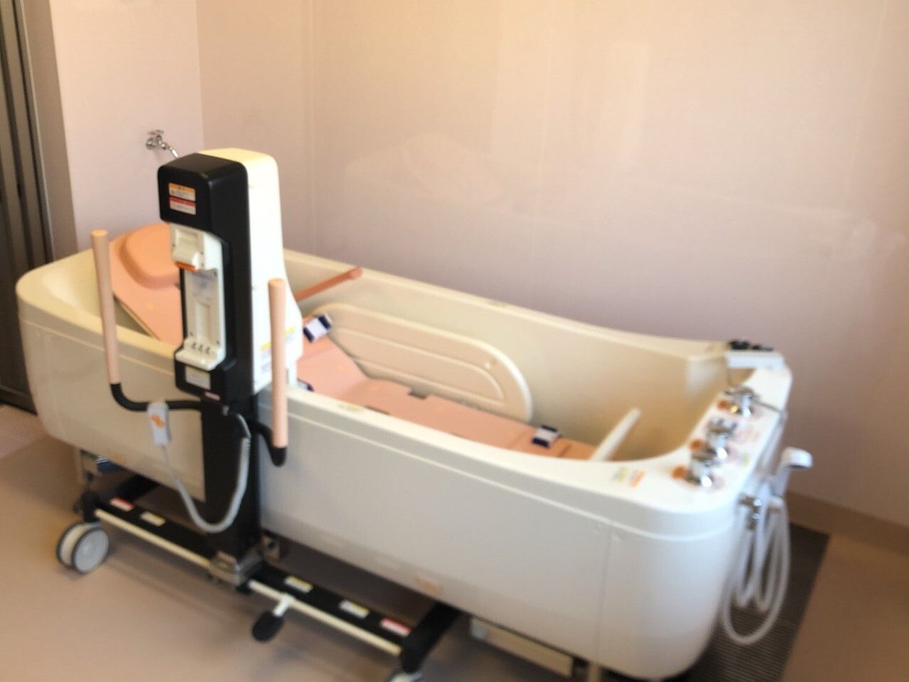 ストレッチャータイプのリフトが設置された箱型の機械。機械のわきにはシャワーも付き、足元にはたくさんのボタンも付いている。