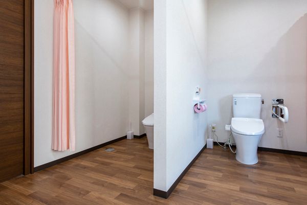 可動式の手すりが付いたトイレは広く、段差もない。トイレが二つ並んでいるがドアはなく、ピンクのカーテンが付いていて、開け閉めができる。