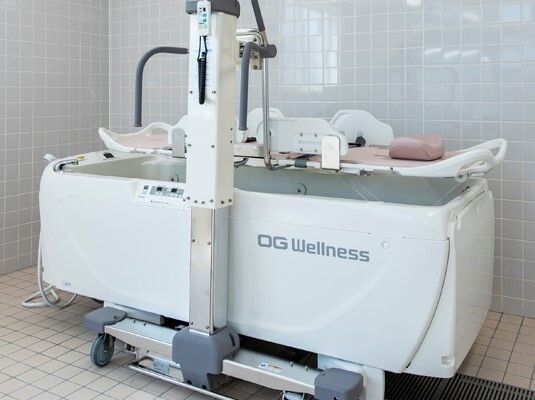 白い箱のような機械にはシャワーが付き、ストレッチャータイプのリフトが設置されていて、リフトに寝たまま浴槽の中に入ることができる。