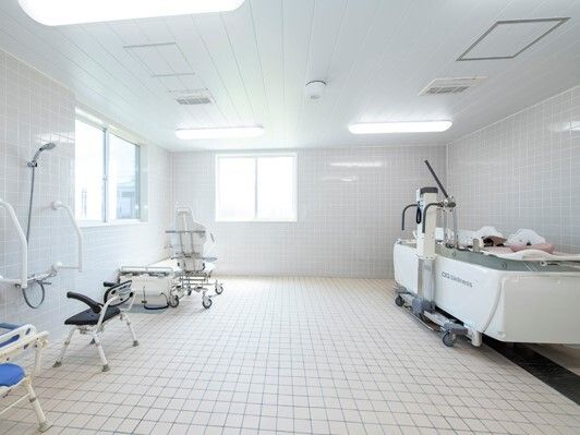 広々とした白を基調とした浴室の右側には寝台浴が設置され、左側にはシャワーチェアが置かれたシャワースペースがあり、奥には座ったまま入浴できる機械がある。