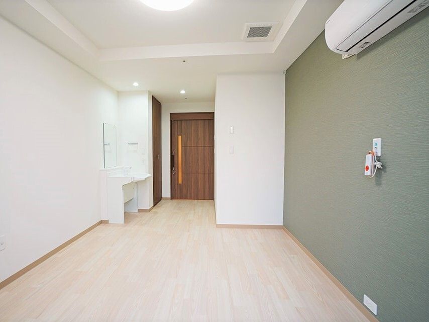 洗面所やエアコン、収納が付いた居室。ダークグリーンの壁には緊急通報装置が設置されている。