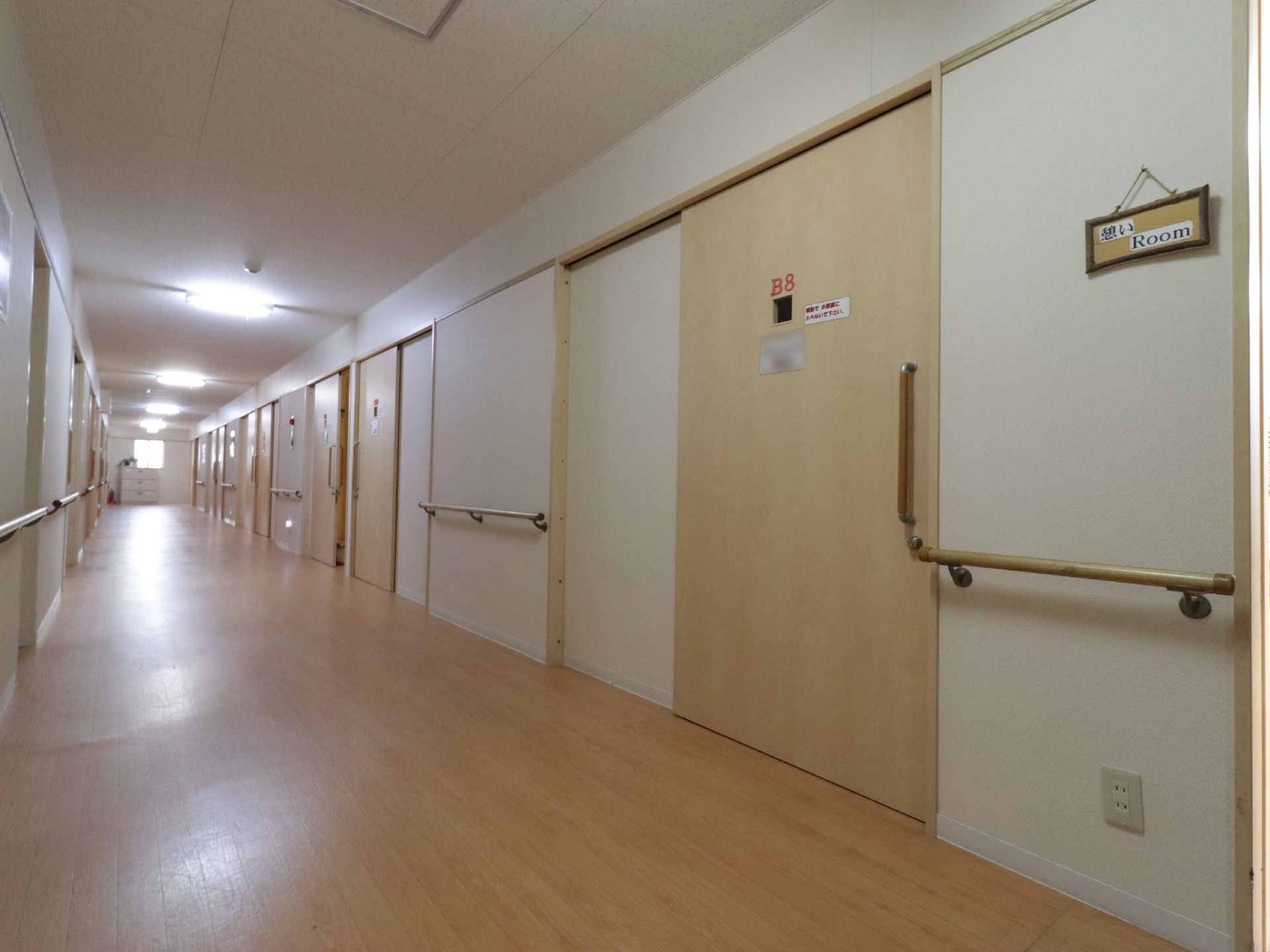 白が基調の明るい広々とした廊下である。居室は大きな引き戸である。両側には手すりが完備されていて安全である。
