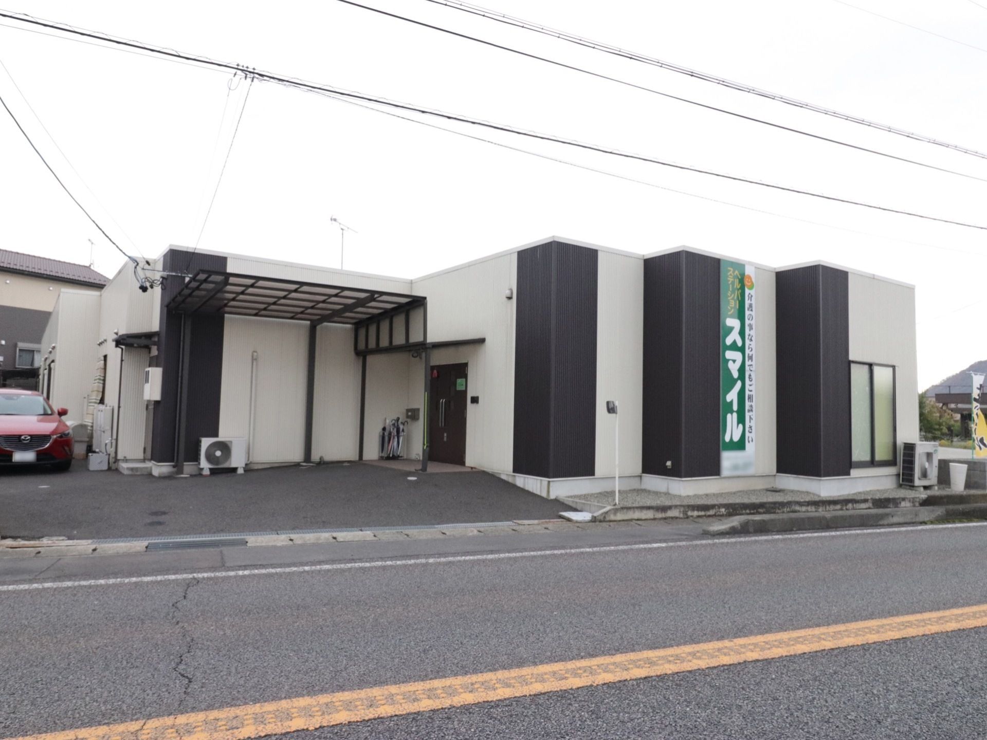 グレーと黒の外壁のモダンな平屋建ての建物になっている。目の前に大きな道路があり、車での来訪も便利になっている。