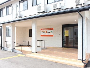 階段と手すり付きのスロープが付いた玄関にはホーム名が書かれている。2階建ての建物は白をメインとしていて清潔感がある。
