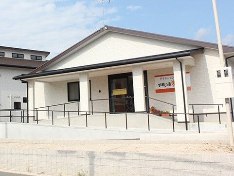 パジャマ姿でベッドに横になっている高齢女性に温かく介護に当たるエプロン姿の女性スタッフ。