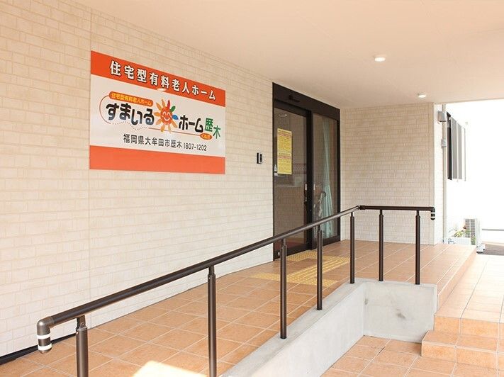 眼鏡をかけた車いすの男性入居者と女性スタッフが屋外での散歩を楽しんでいる。