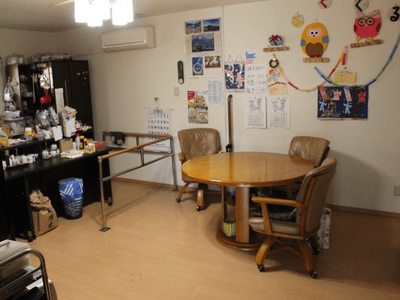 片付きすぎていない家庭的な雰囲気の共有スペース壁にはカレンダーや手作りの飾りが飾られ、木製のテーブルセットが置かれている。