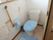 ボタン式の呼び出し機器が付いたトイレ。木目調の手すりが付き、ブルーのトイレカバーが付けられている。出入り口は引き戸。