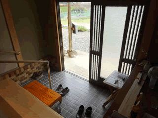 無造作に靴が数足脱ぎ捨てられている玄関には手すりや台が設置され、家庭的な雰囲気。靴箱の上には装飾品も置かれている。