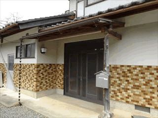 レトロな雰囲気が漂う民家風の建物。玄関にはシルバーのポストが設置され、きれいに片付けられている。玄関のドアは少し幅が広い。