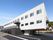 白を基調とした３階建ての建物。玄関先には屋根が付き、ベランダもあり、明るい雰囲気。