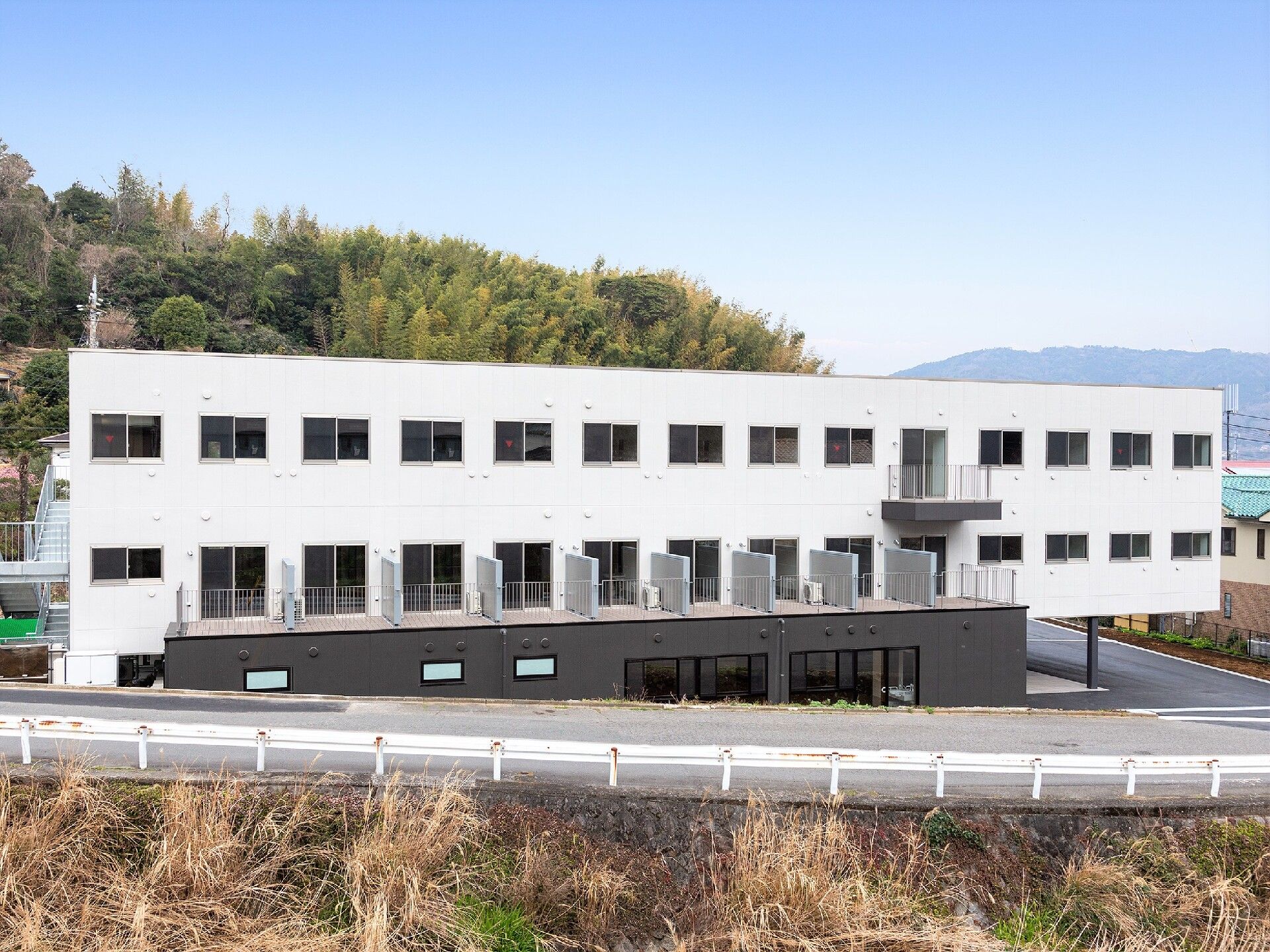 白を基調とした3階建ての建物。側面にはベランダが付き、広い駐車スペースもある。