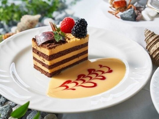 四角く切られたケーキの写真。上にベリーが乗っていて手前にソースで飾り付けがしてある