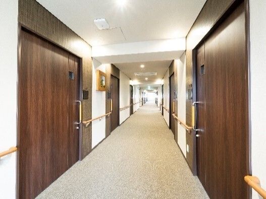 寝具付きのベッドが設置されたフローリングの部屋にはエアコンや洗面所が付き、木製のチェストの上には小さな観葉植物が並び、いすやテーブルもある。