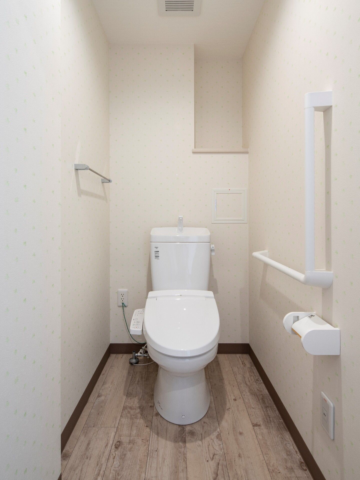 温水便座が設置されたトイレはシンプルな造り。右上にはオープンタイプの棚があり、壁にはタオル掛けやトイレットペーパーホルダー、手すりがある。