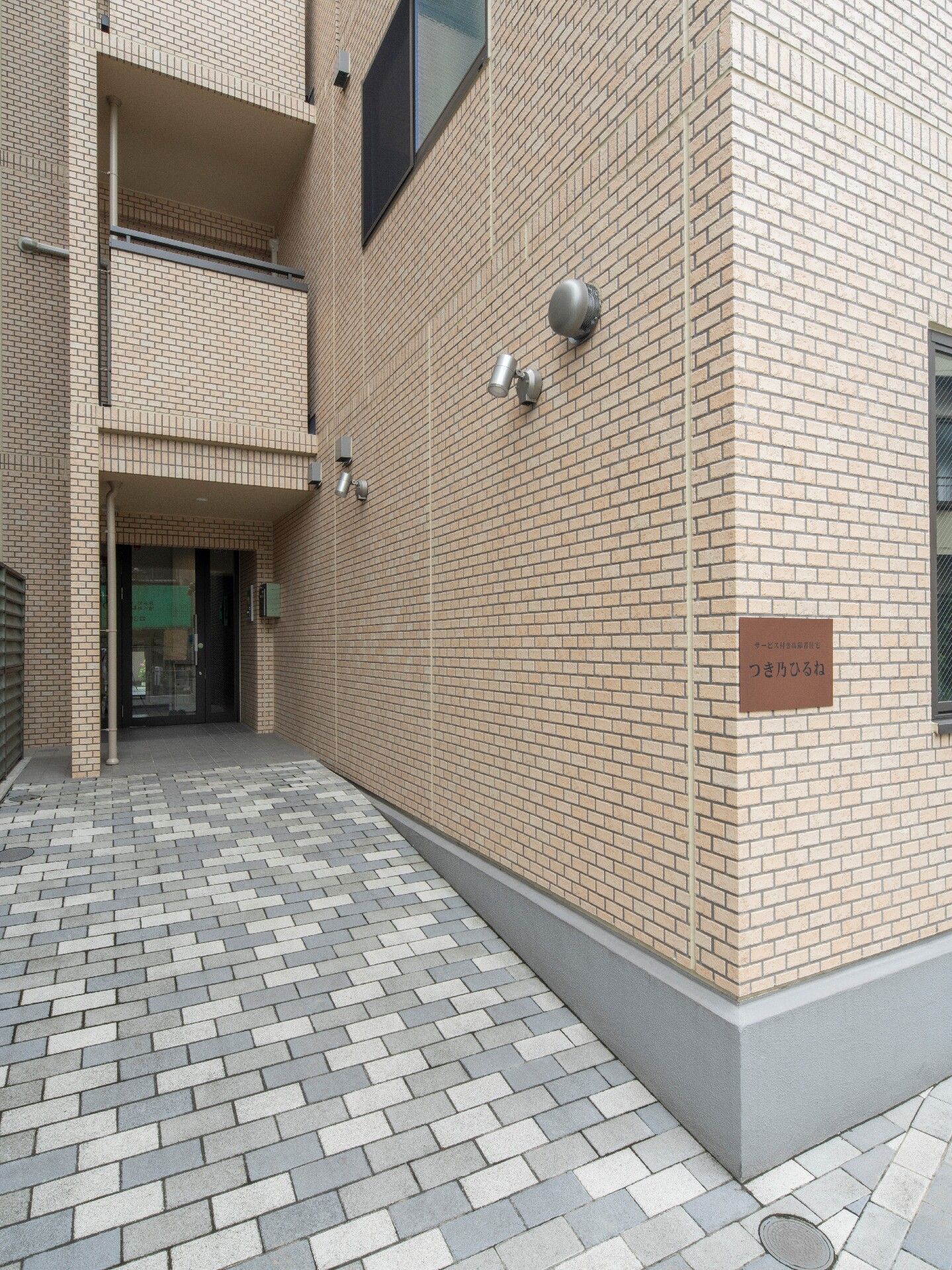 玄関部分は少し奥まったところにあり、屋根が付いている。玄関周りにはグレーと白のブロックが敷かれ、段差が解消されている。