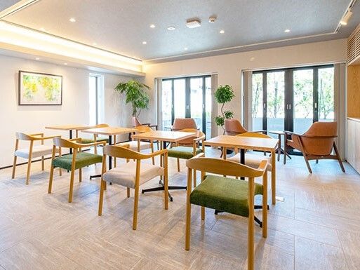 カフェのような共有スペース。木製のダイニングテーブルが複数置かれ、絵画も飾られ、明るい雰囲気。
