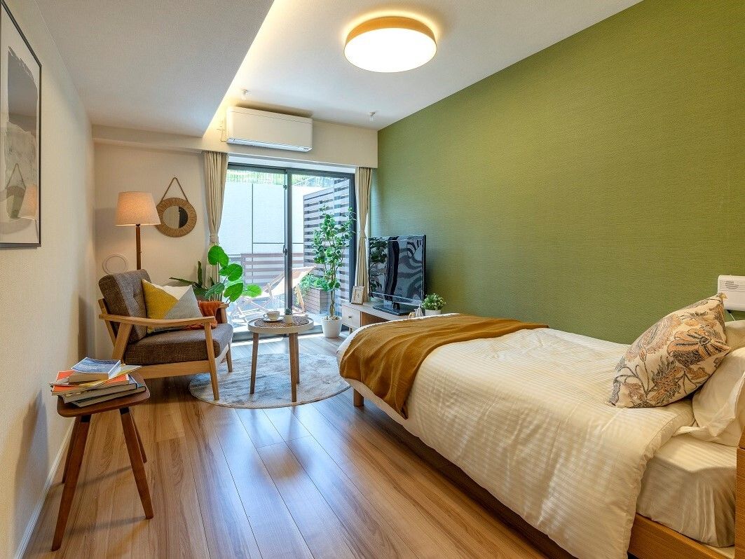 エアコン付きのフローリングの部屋には寝具付きのベッドが置かれ、観葉植物やテレビも置かれている。