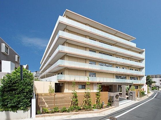 日当たりのいい場所に建っている白と黄色の5階建ての建物。周りには緑が植えられ、フェンスもある。