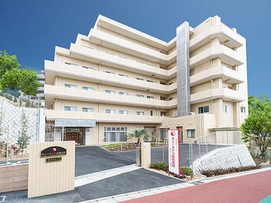 ベージュの6階建ての建物周りには緑が多くあり、敷地内にも菜園らしきスペースがある。