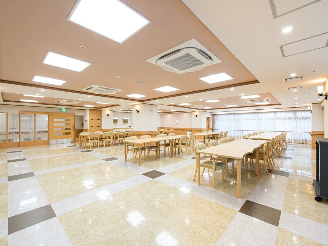 木製のダイニングテーブルセットが複数置かれた食堂は明るい雰囲気。大きな窓にはカーテンが付いている。