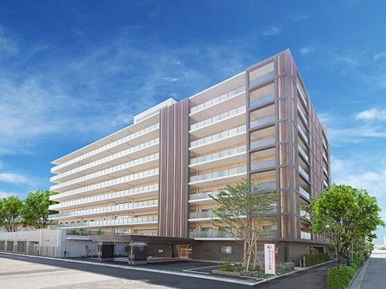 駐車場があり、草木が植えられている。建物は大きく、都心のマンションのような外観。