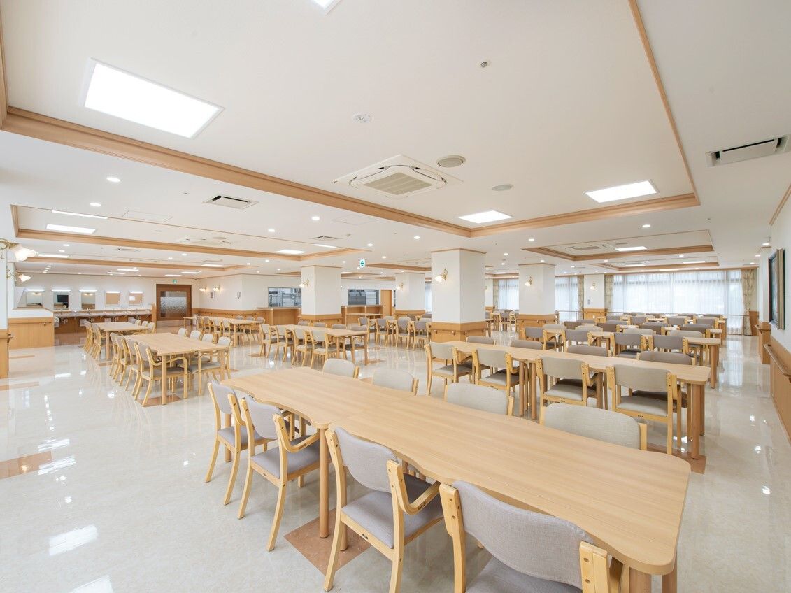 木製のダイニングテーブルセットが複数置かれた食堂は明るい雰囲気。奥には大きな窓がある。