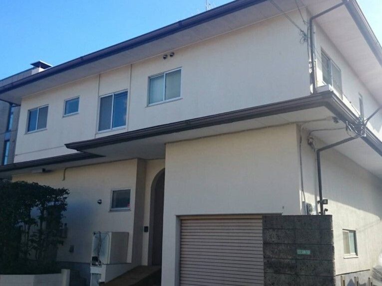 2階建ての建物は白い外壁で日当たりのいい場所に建っている。玄関周りには草木が植えられている。