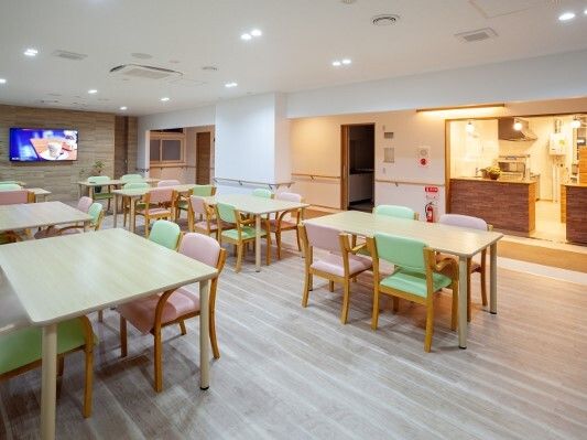 パステルカラーの椅子がセットされたダイニングテーブルが複数置かれた食堂には、大きな壁掛けテレビも付いている。