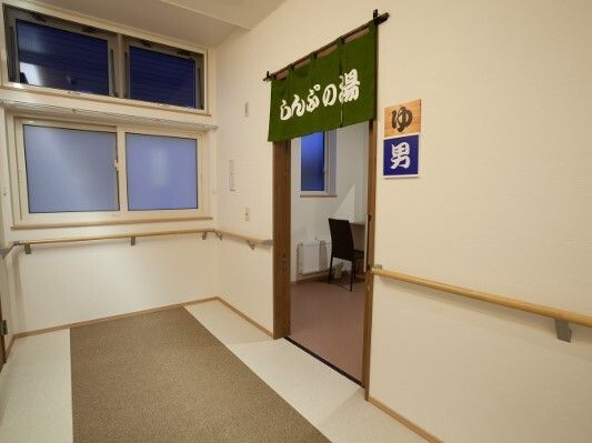 手すりが付いた廊下の一角に浴室の入り口があり、のれんや「男」「ゆ」と書かれたステッカーが貼られている。