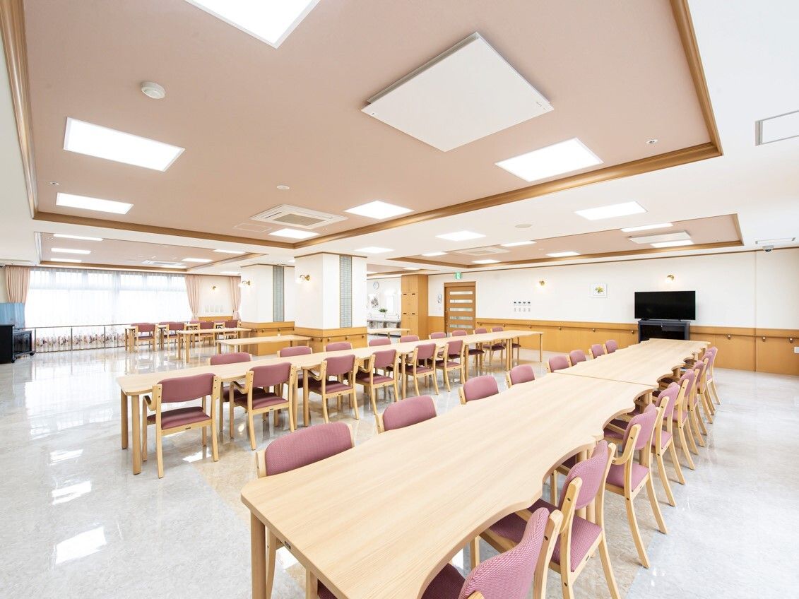 ピンクの椅子がセットされた木製のダイニングテーブルセットが複数置かれた食堂は明るい雰囲気。