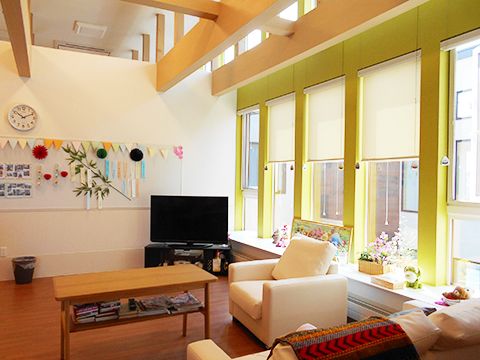黄色い枠の大きな窓が付いたリビングにはテレビやソファがあり、壁には手作りの笹飾りや笹の枝が飾られている。