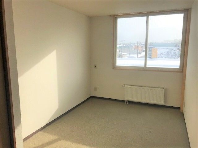 パネルヒーターが付いた居室。カーテンが付いていない大きな窓があり、家具もまだ置かれていない。