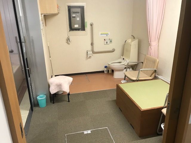 左側には浴室につながるドアがあり、広い脱衣所には小上がりのスペースやいす、カーテンが付いているトイレがある。
