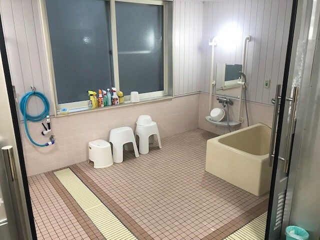 大きな窓が付いた浴室は洗い場が広く、右端に一人用の浴槽とシャワーが設置され、デザインの異なる浴室用の椅子がある。