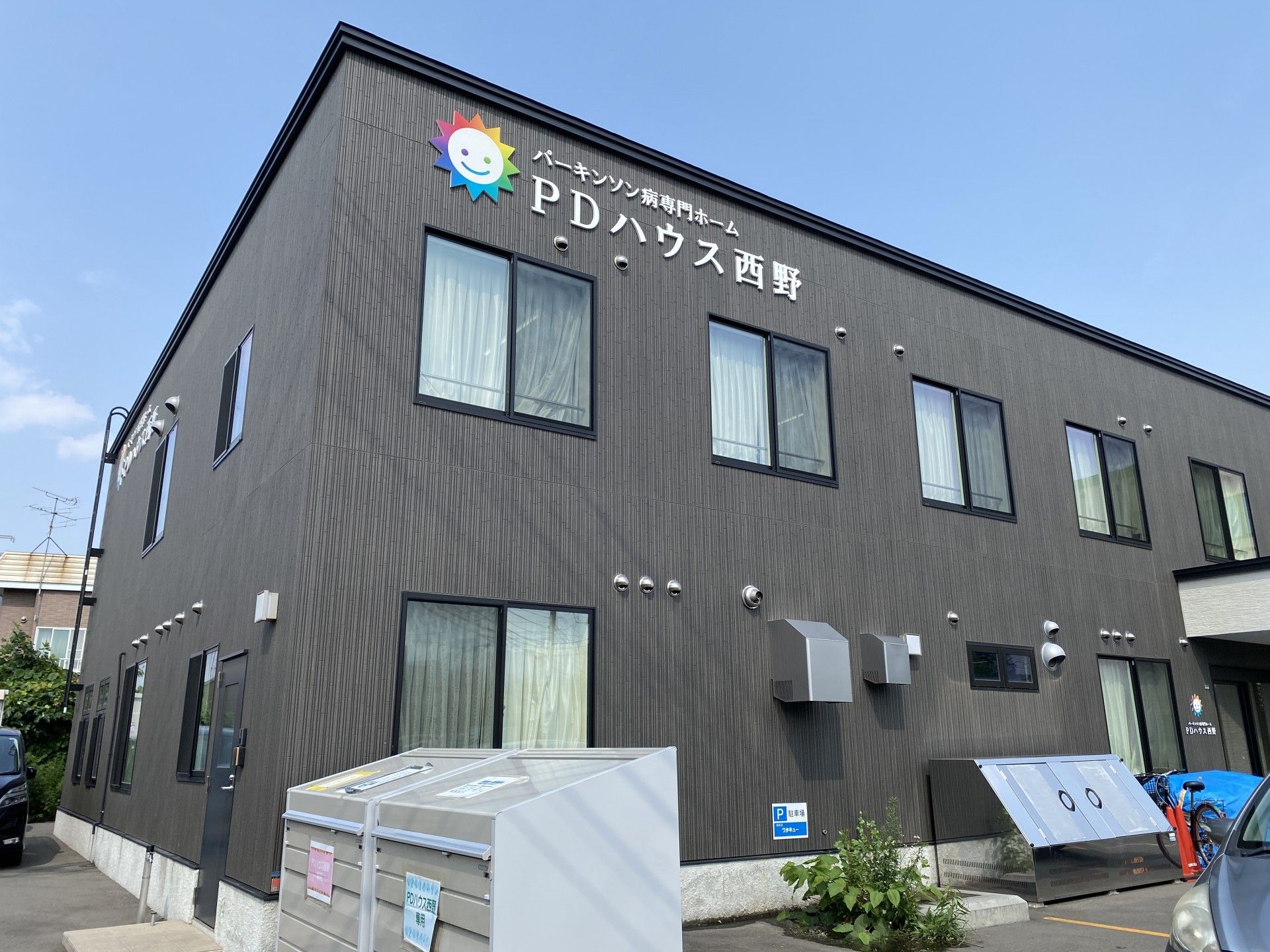 ダークグレーの2階建ての建物は広い駐車場があり、外壁にはホーム名が書かれている。日当たりのいい場所。