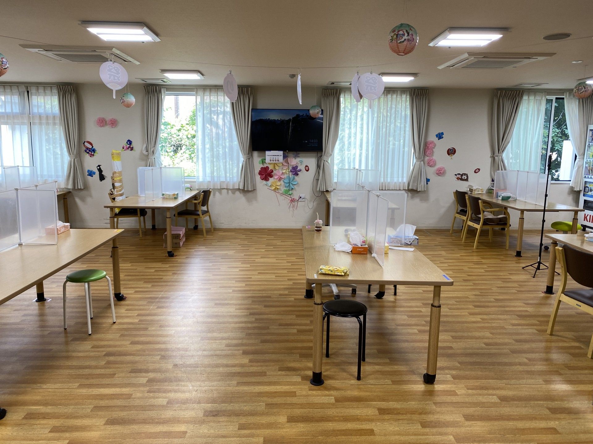 緑の多い屋外でブルーのポロシャツを着た若い女性スタッフに付き添われて、外気浴を楽しんでいる車いすの高齢女性。