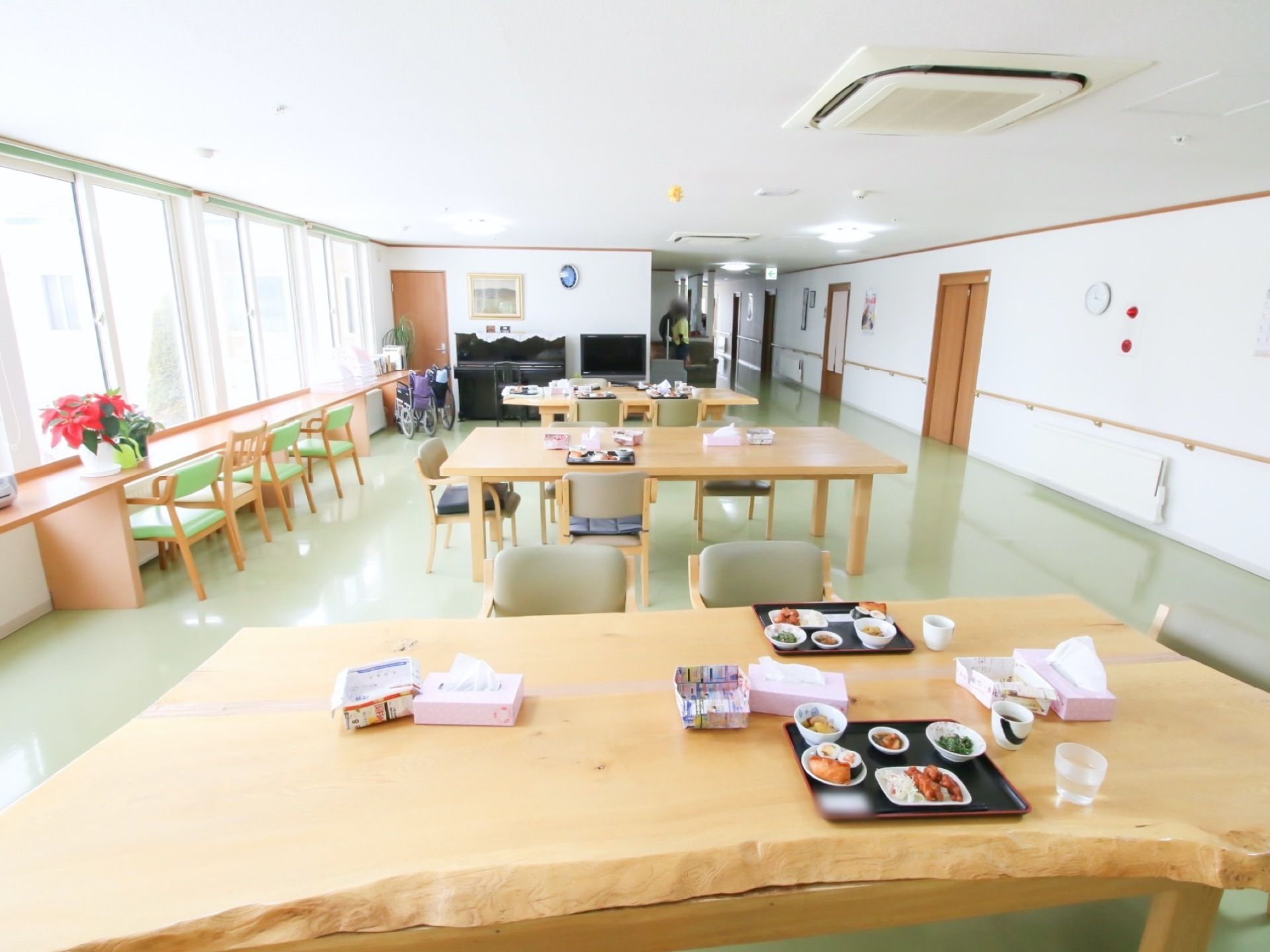 食堂のテーブルの上に、料理の乗ったトレーが置かれている。窓から明るい日差しが入っている。正面にテレビとピアノがある。
