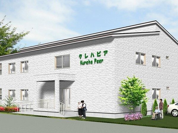 ホーム名が書かれている白を基調とした２階建ての建物は日当たりがよく、スタッフに付き添われた高齢女性が玄関の近くにいる。
